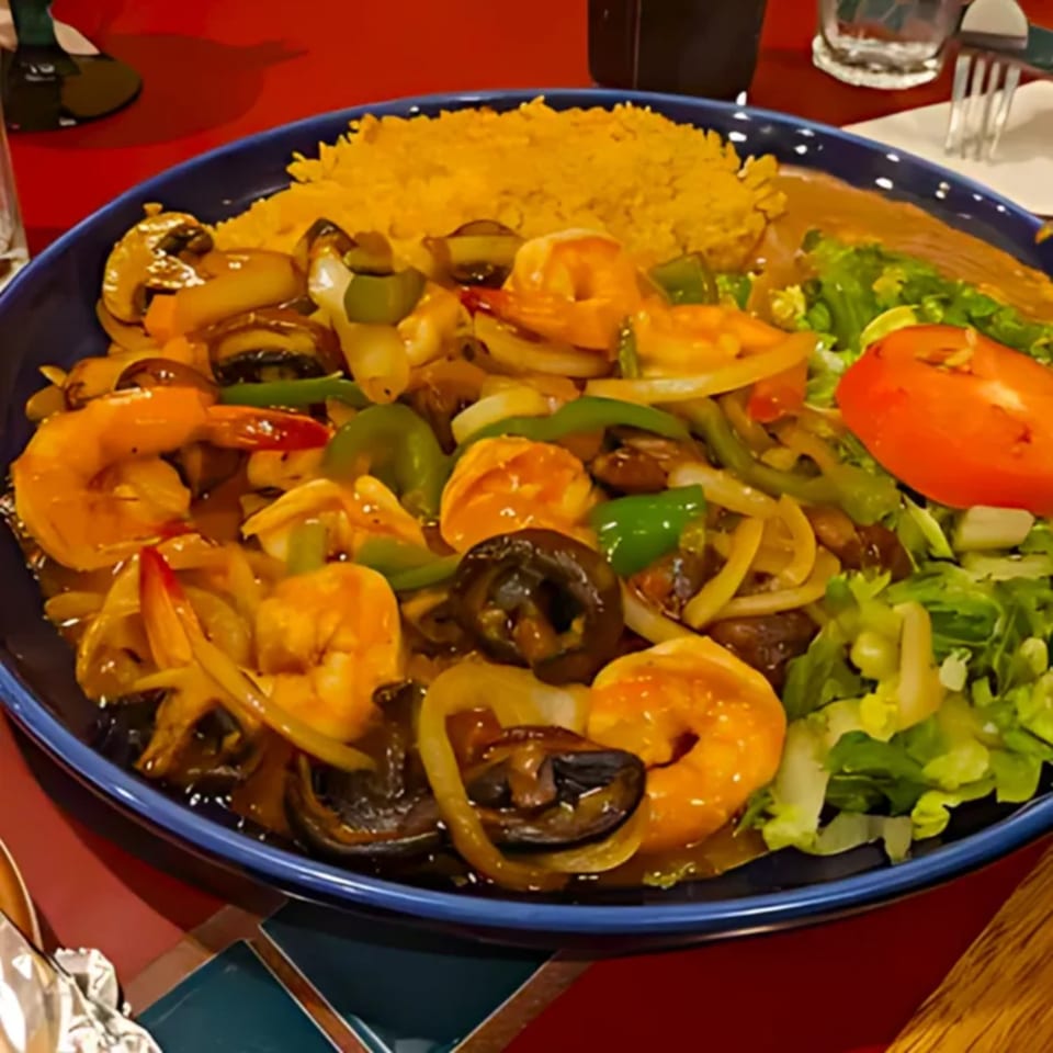 A vibrant Mexican shrimp fajita with rice, beans, and salad on a blue plate.