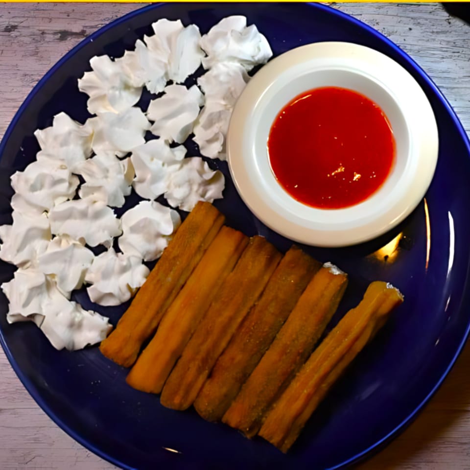 A blue plate holds churros, whipped cream, and a bowl of red dipping sauce.
