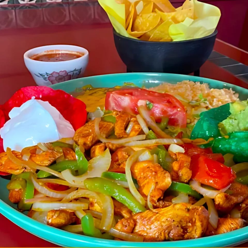 Chicken fajitas with bell peppers, onions, rice, guacamole, sour cream, salsa, and tortilla chips.