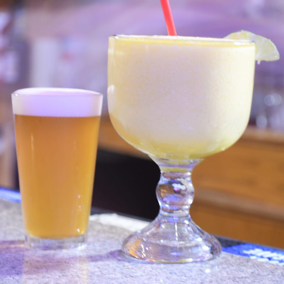 A frosty margarita with a lime wedge and a glass of beer on a bar counter.