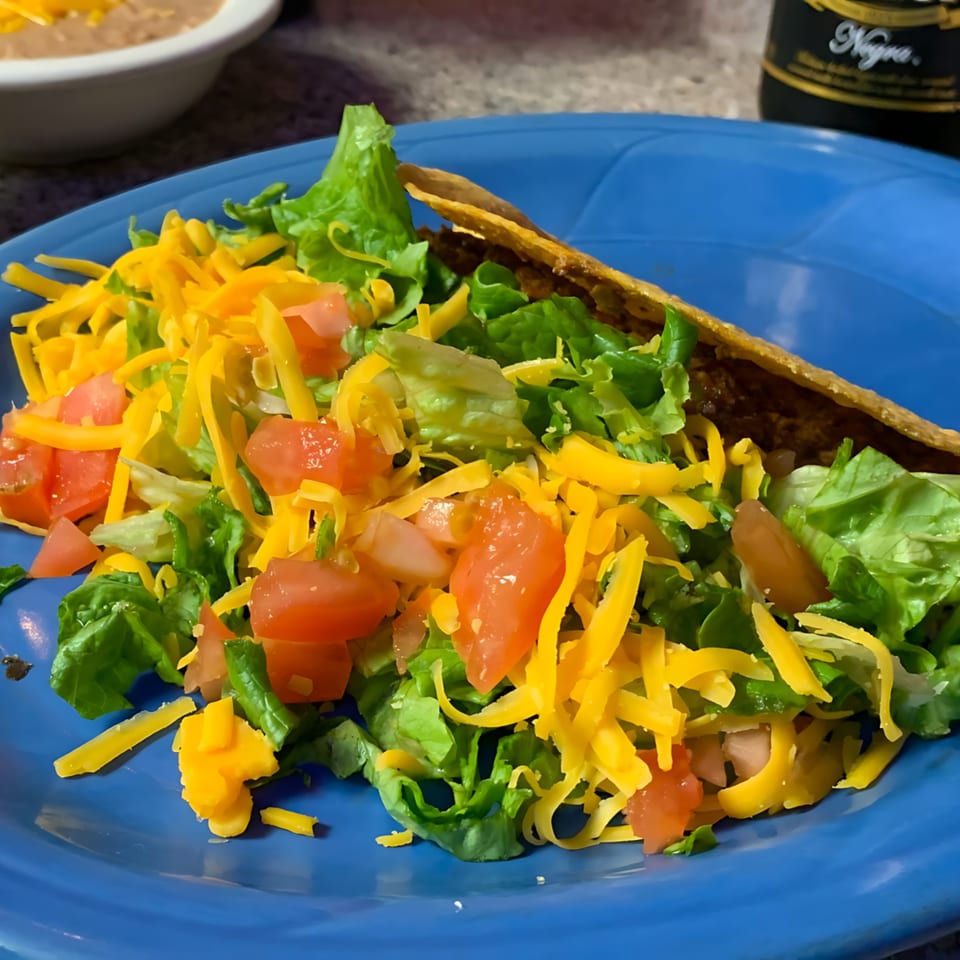 A crispy taco shell filled with ground beef, topped with lettuce, shredded cheese, and diced tomatoes.
